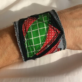 Blue denim wrist cuff, abstract appliqué pattern, red and green.