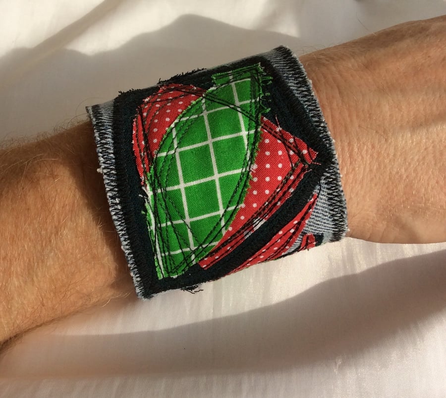 Blue denim wrist cuff, abstract appliqué pattern, red and green.