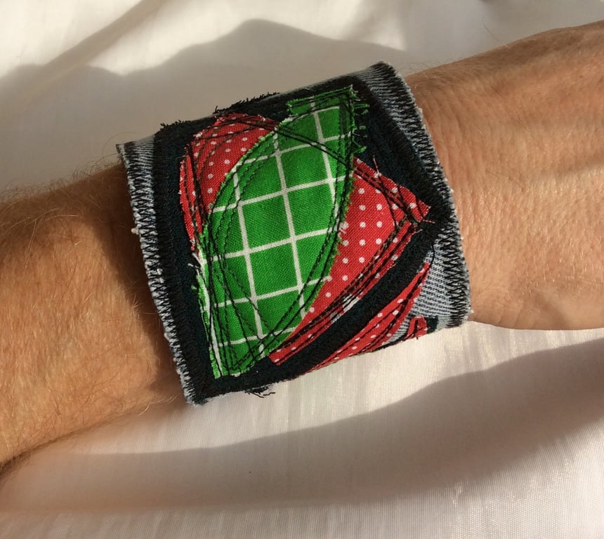 Blue denim wrist cuff, abstract appliqué pattern, red and green.