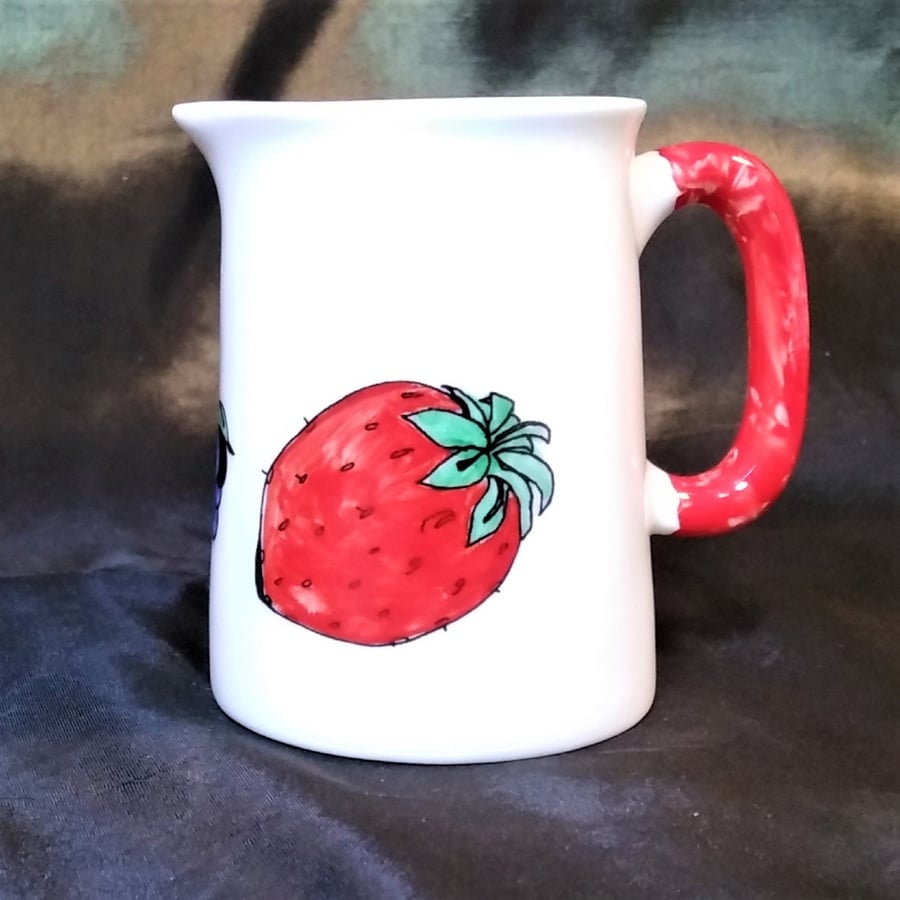 Milk jug in fine white bone china decorated with fruit and a red handle