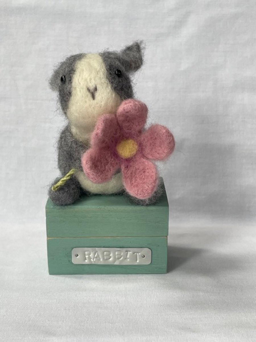 Handcrafted needle felted rabbit holding a flower on a wooden box