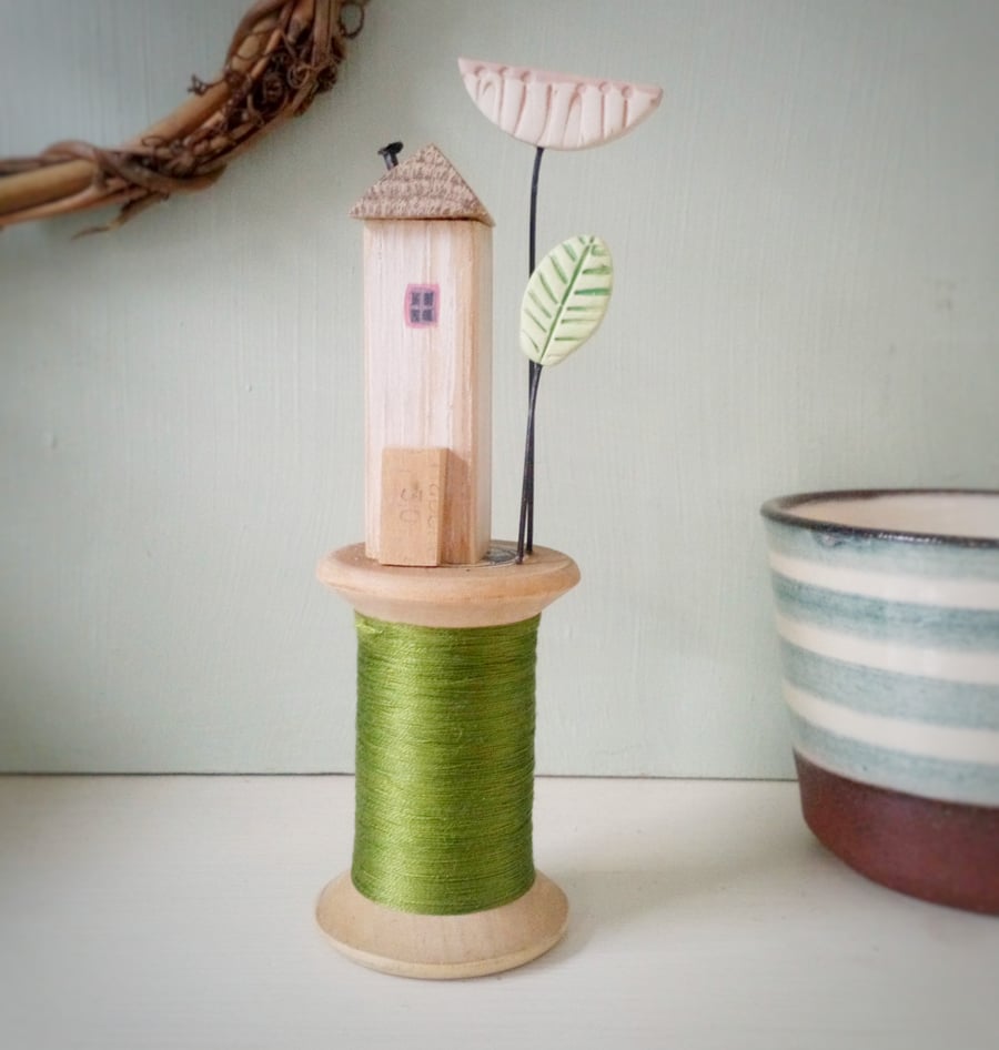 Tiny oak house with clay flower on vintage wooden bobbin