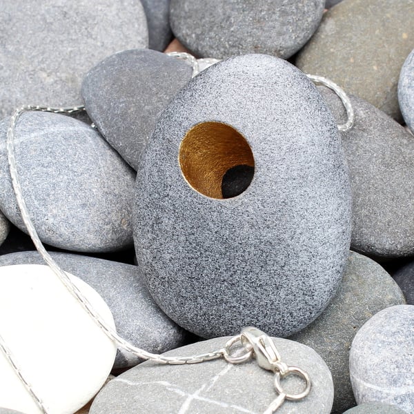 A Pebble pendant with a gilded hole that goes through the pebble. Silver chain