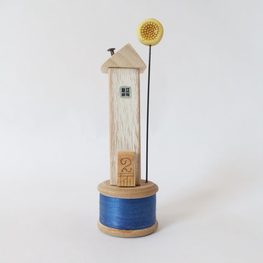 Wooden house with clay sunshine flower on a vintage wooden bobbin