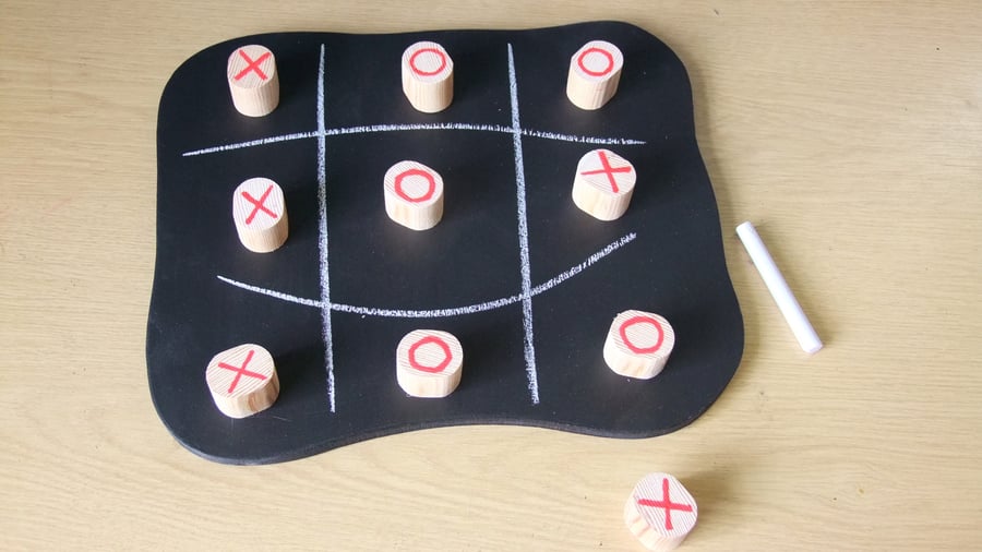 Noughts & Crosses game on a wooden chalk board with large wooden pieces.