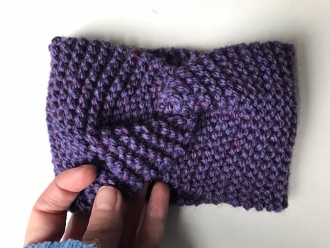 A hand knitted purple mix headband with a decorative twist