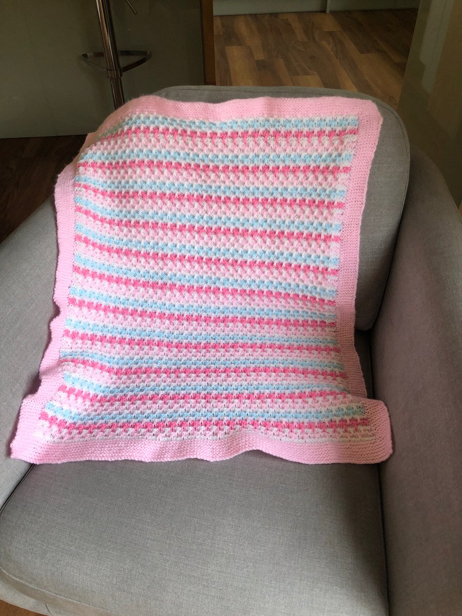 Pink hand knitted pushchair blanket.