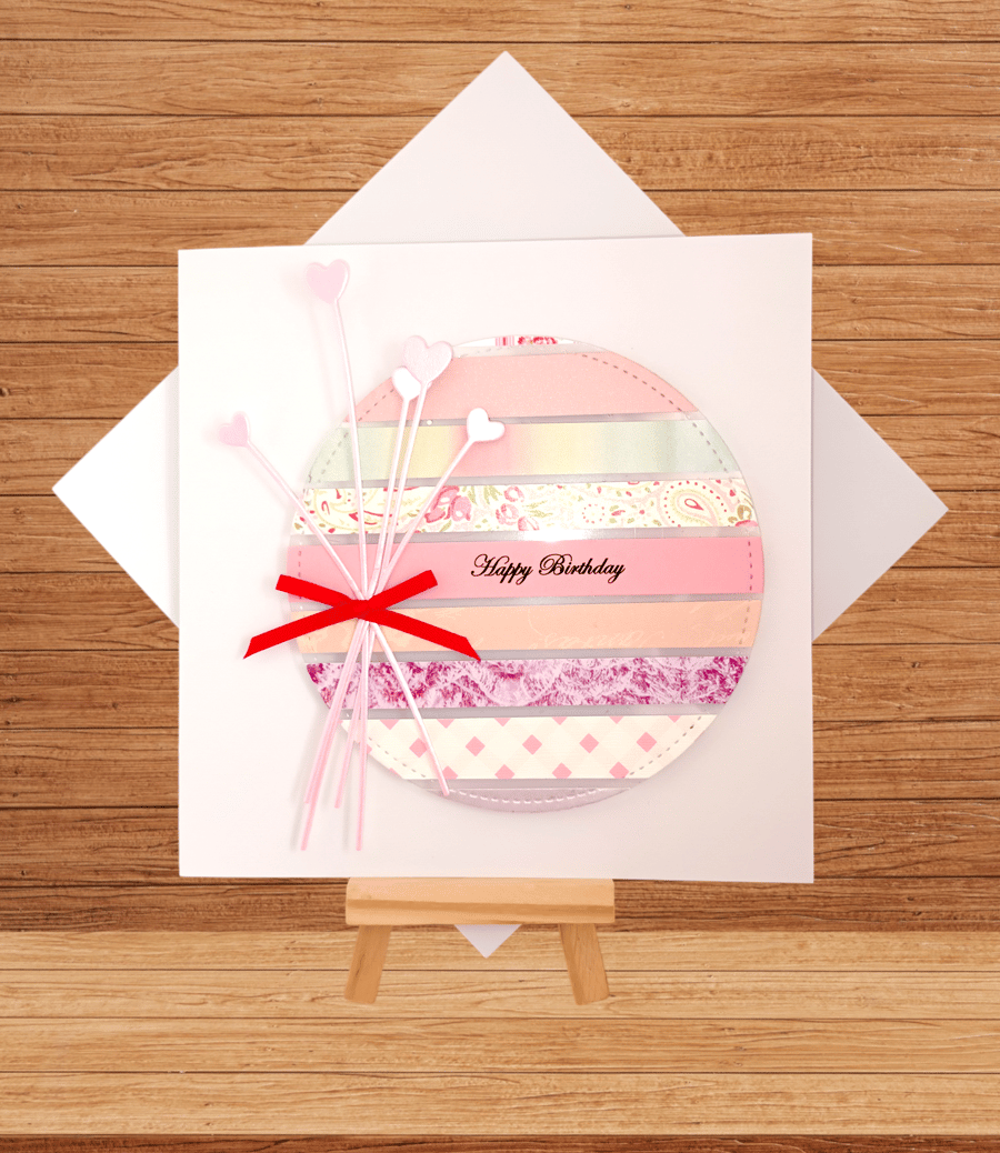 Striking striped pink tone birthday card with heart flower decoration..