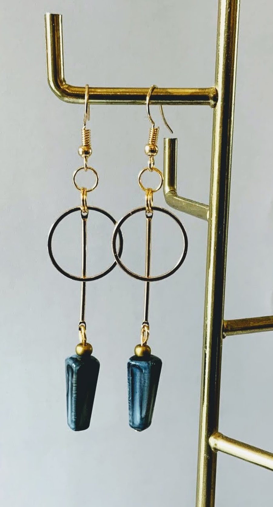 Gold hoop earrings with hanging rod and teal geometric bead.