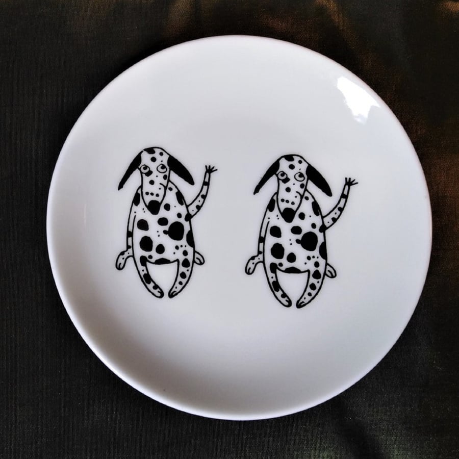 Twin Dalmatians sitting side by side on a small shallow dish, decorated with two