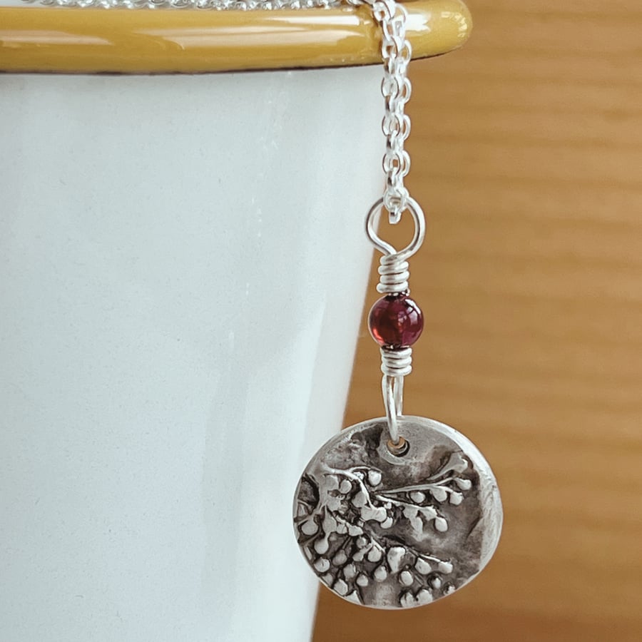 Botanical silver pendant with  sambuca plus a garnet bead , on silver chain.