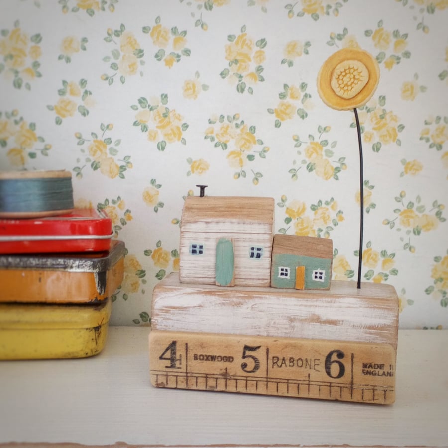 Little wooden houses with clay sunflower on a vintage ruler block