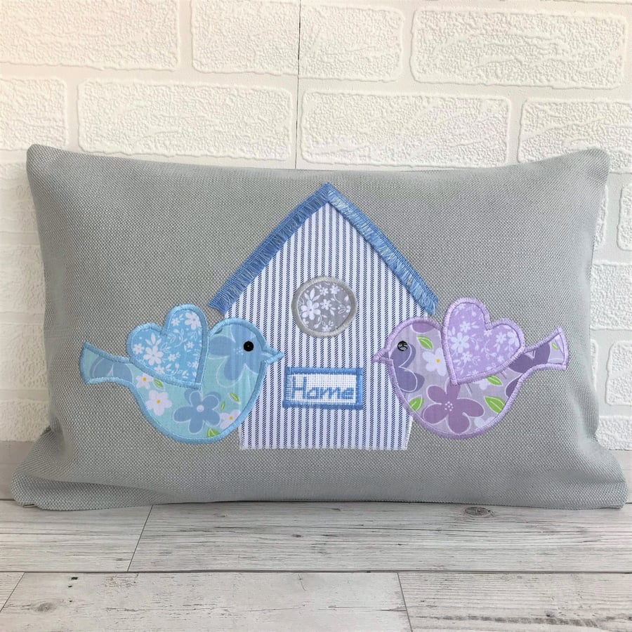 Grey rectangular cushion with blue and lilac floral birds and striped birdhouse