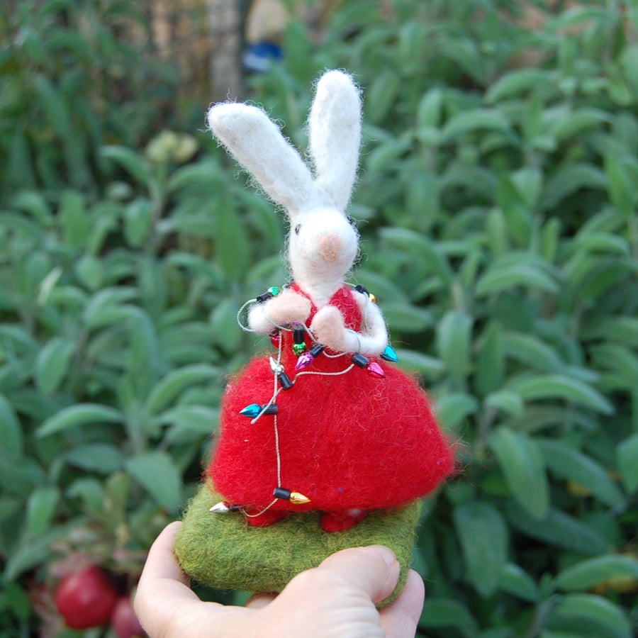 Needlefelt white rabbit wearing a red dress and holding Christmas Lights