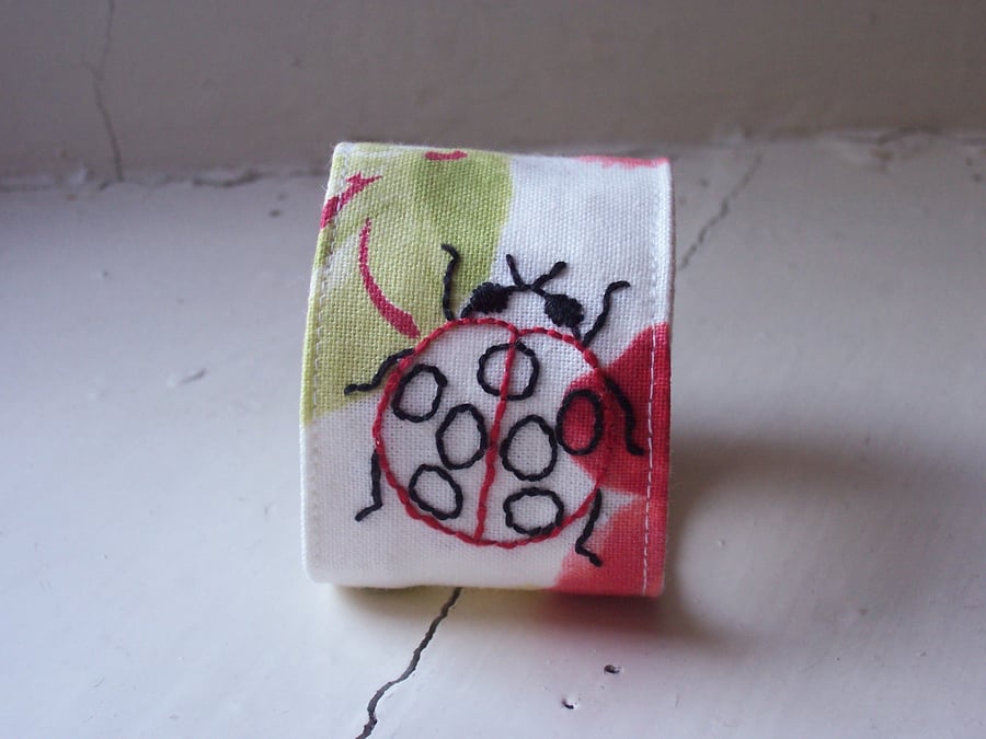 Hand embroidered textile cuff with ladybird and poppies
