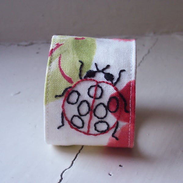 Hand embroidered textile cuff with ladybird and poppies