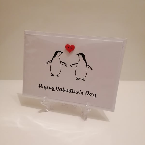 Happy valentines Day greetings card with two penguins and a red heart button