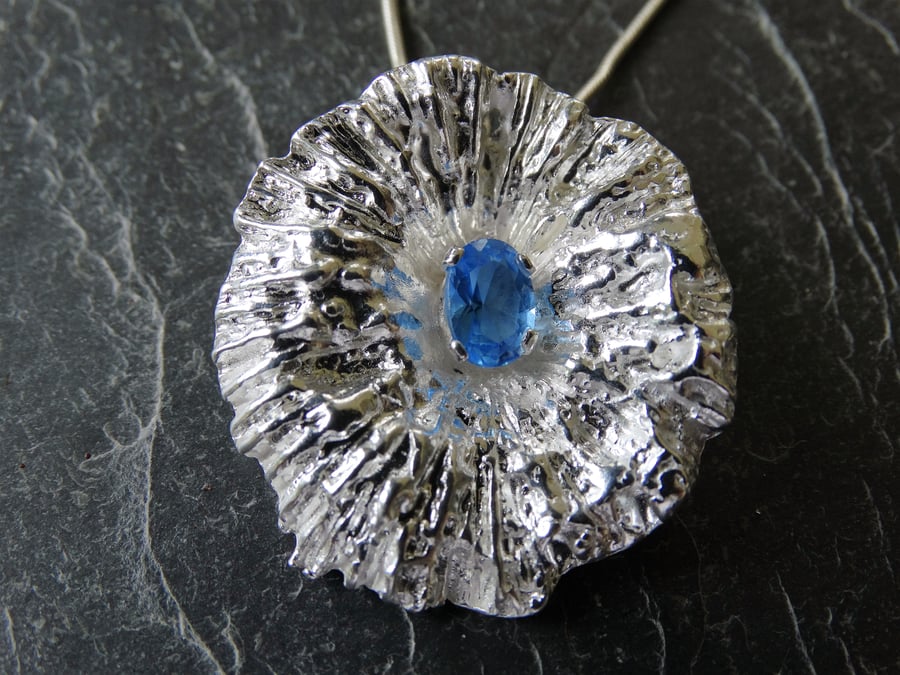 Sterling silver cast coral pendant. Set with faceted blue topaz