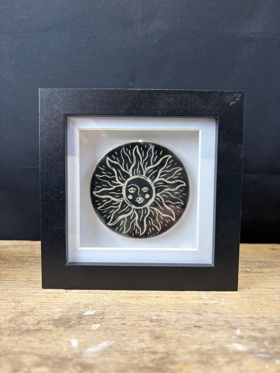 Ceramic tile with 'sun face' design presented in black shadow box frame