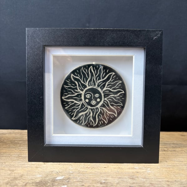 Ceramic tile with 'sun face' design presented in black shadow box frame