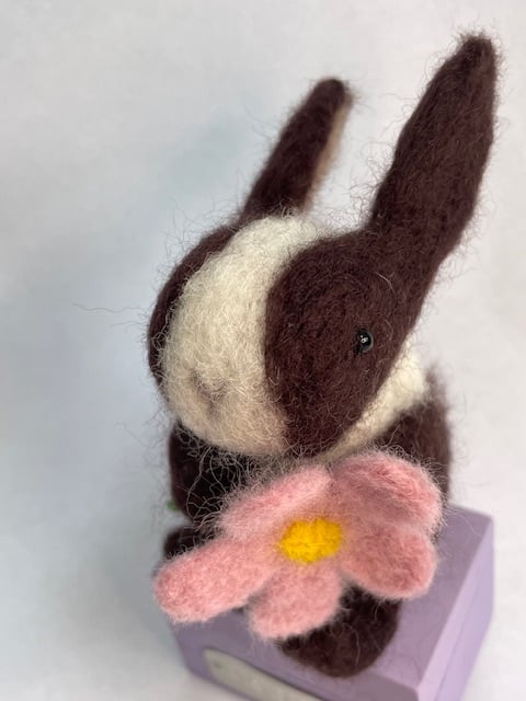 Handcrafted needle felted rabbit holding a flower on a wooden box