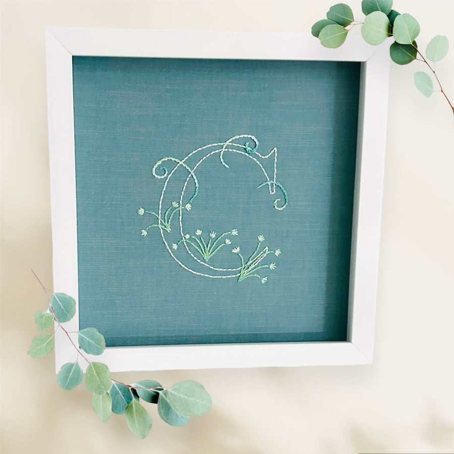 A framed embroidered monogram of The initial C designed with flowers.