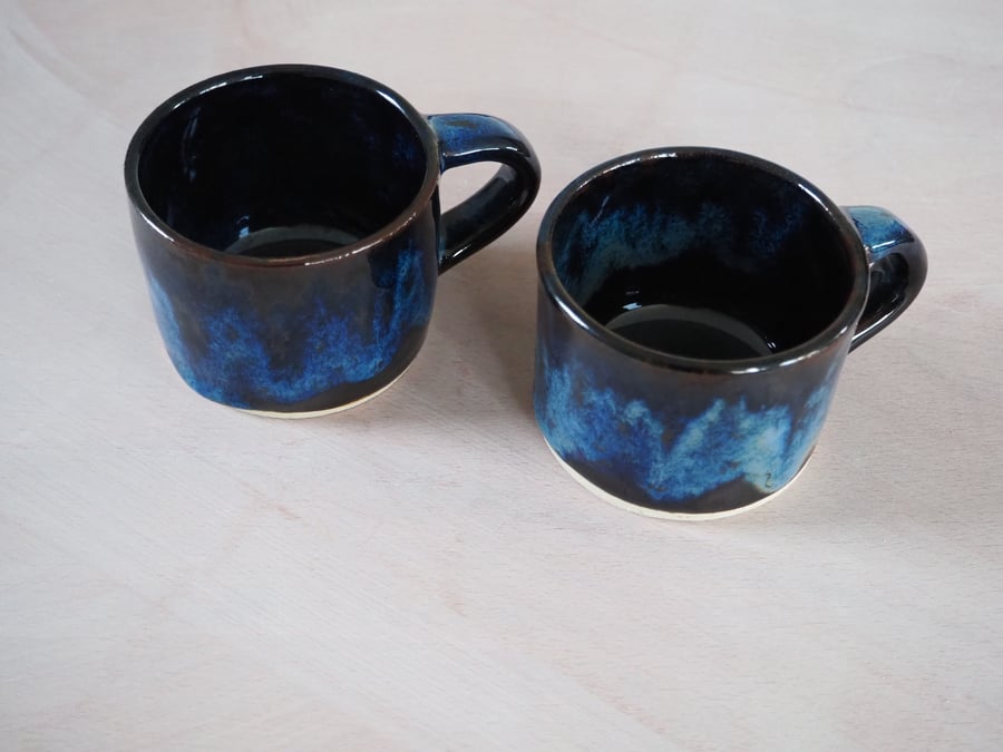 Set of two pottery mugs finished in blue and black glaze combination.