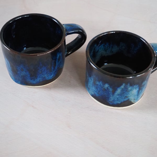 Set of two pottery mugs finished in blue and black glaze combination.