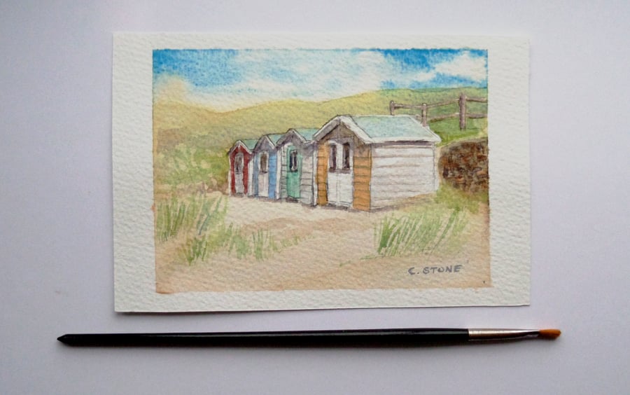 Small watercolour painting of beach huts on a sandy beach 