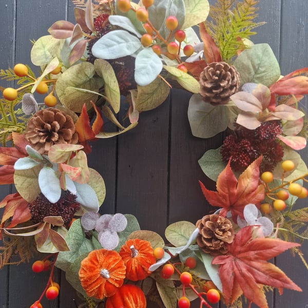 Autumn wreath with plush orange pumpkins, pinecones, berries and mixed foliage. 