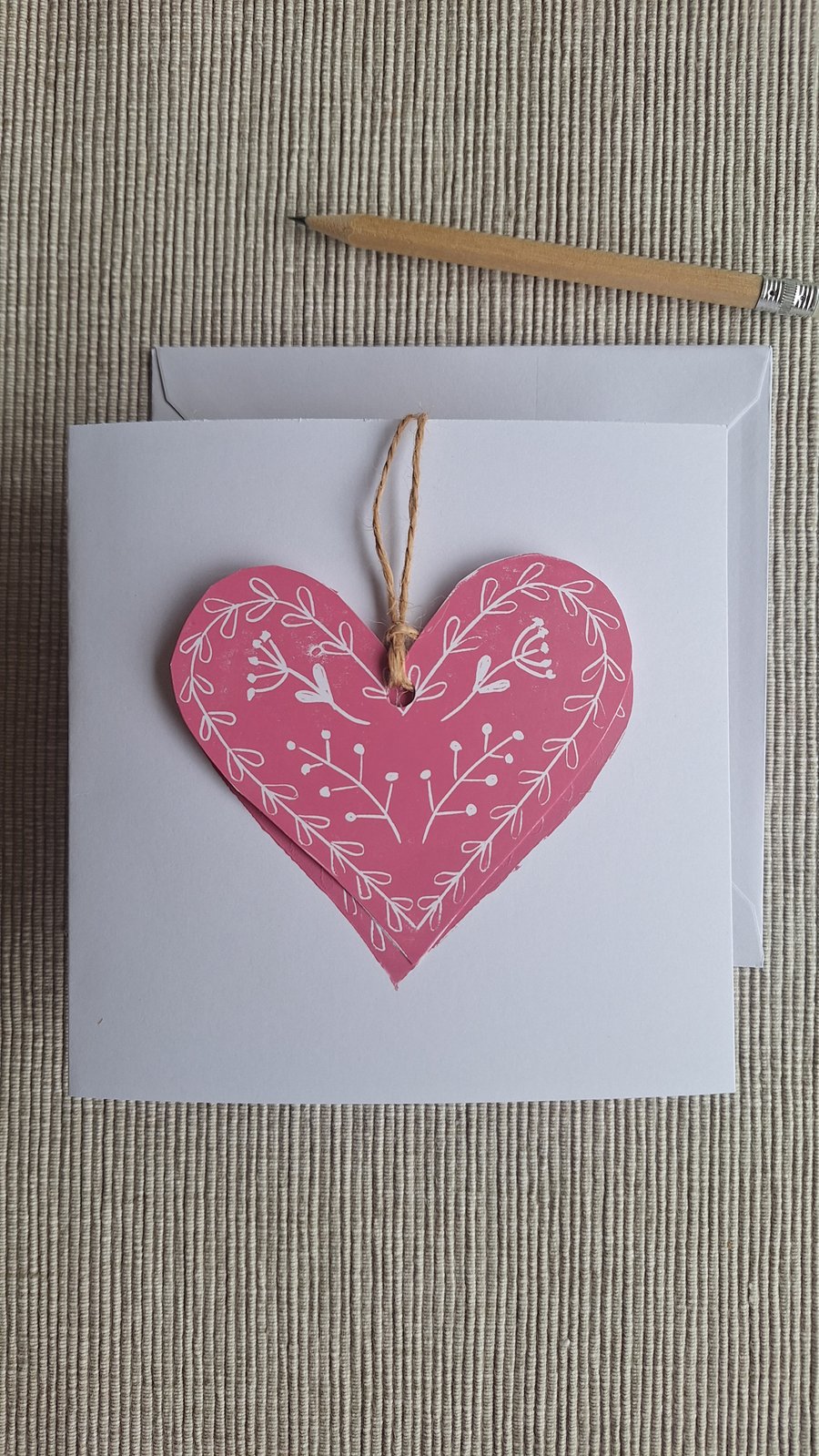 Linoprinted greetings card featuring heart and attached heart decoration.