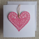 Linoprinted greetings card featuring heart and attached heart decoration.