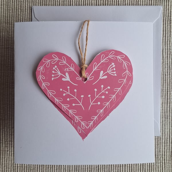Linoprinted greetings card featuring heart and attached heart decoration.