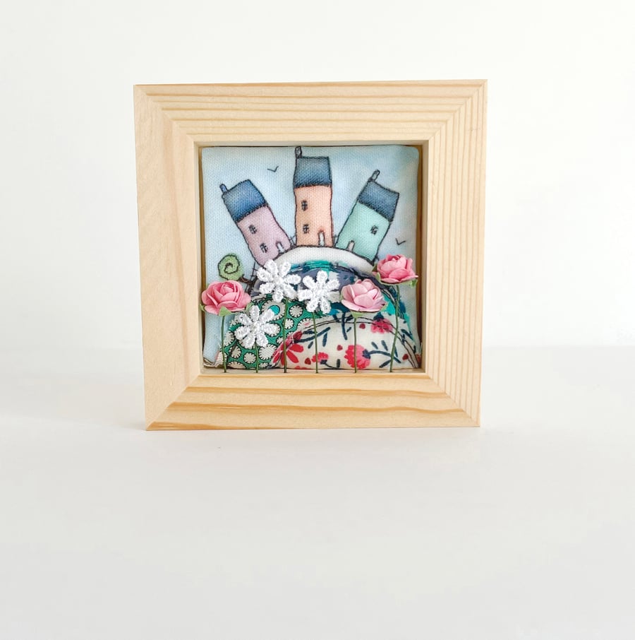 Little houses on a fabric hill, with flowers, in small wooden frame