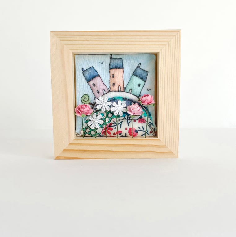 Little houses on a fabric hill, with flowers, in small wooden frame