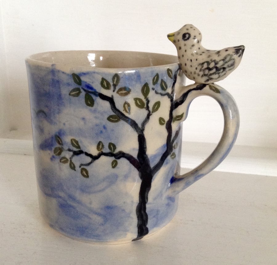 Mug with tree design, blue sky and sculpted bird on the handle. Free UK postage