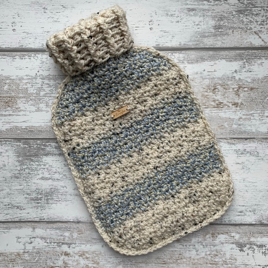 A hot water bottle and handmade crochet cover in blue and cream tweed
