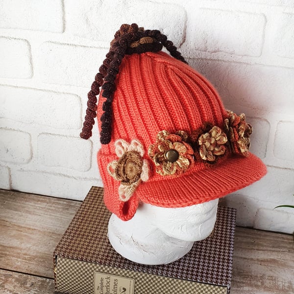 Orange helmet style crochet hat with beige crochet flowers and crochet tail