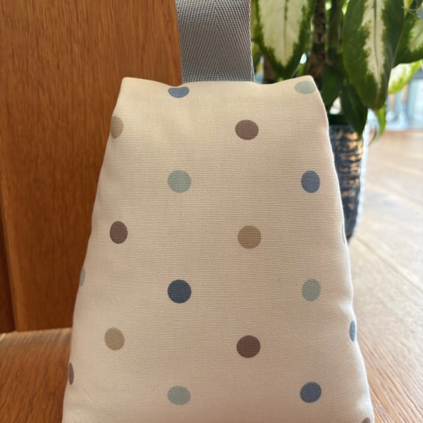 Cotton fabric doorstop in cream with pastel polka dots, filled with pebbles.