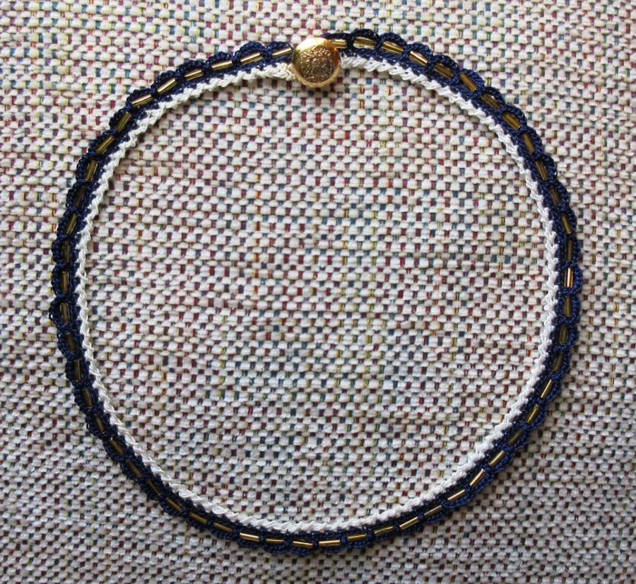 A crocheted necklace in navy blue and cream crochet cotton with gold bugle beads