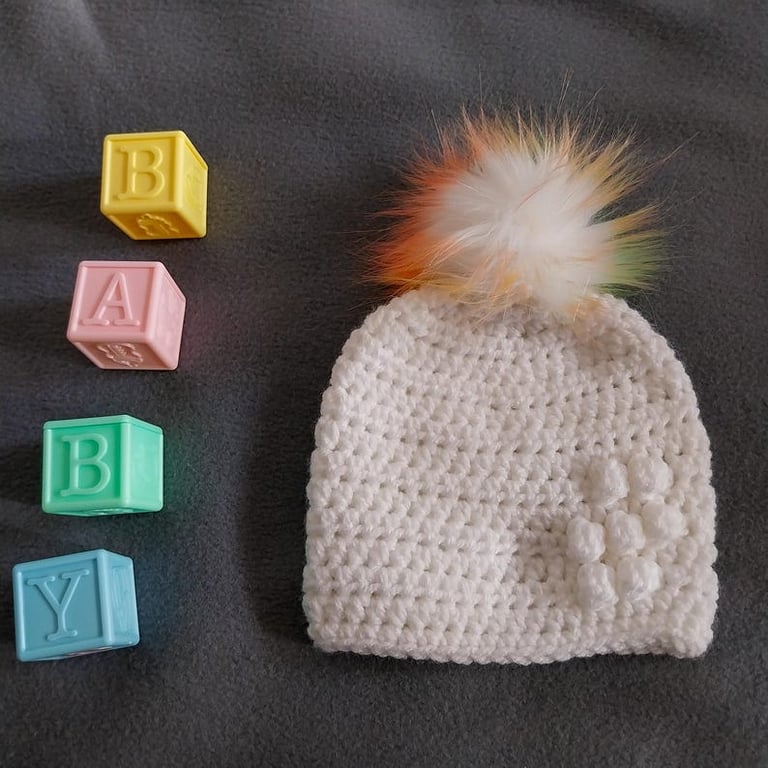 White baby crocheted hat white faux fur pompom with orange yellow & green 