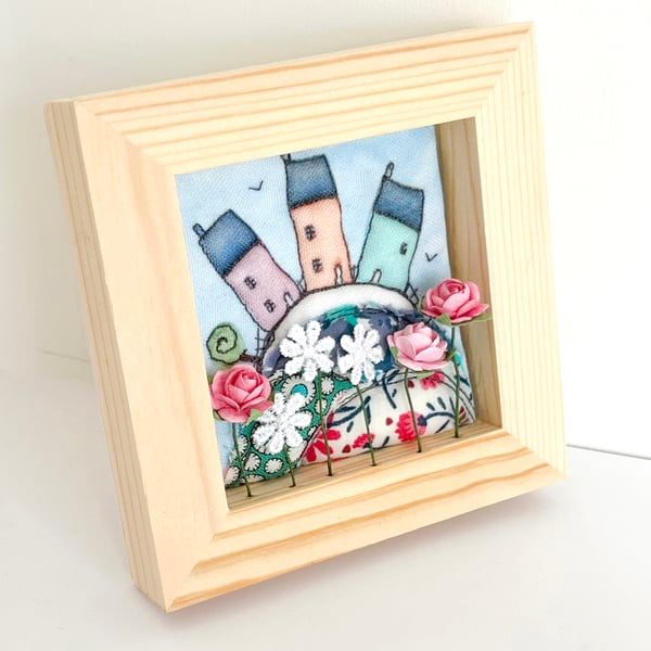 Little houses on a fabric hill, with flowers, in small wooden frame