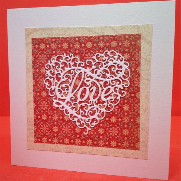 Handmade valentines card, with white papercut heart on a red flowered background