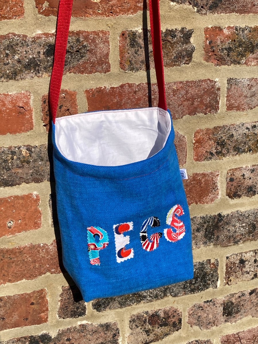 Blue peg bag with red shoulder strap. 