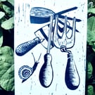 A freshly printed linocut greetings card featuring garden tools