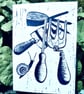 A freshly printed linocut greetings card featuring garden tools