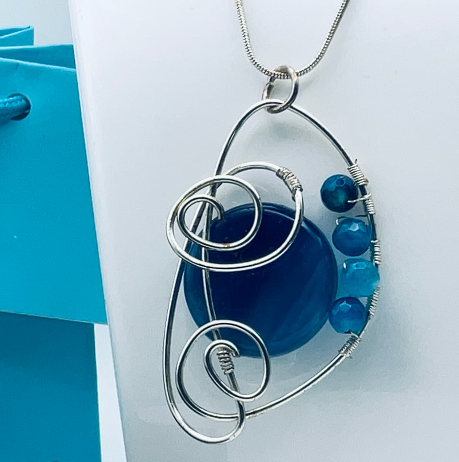 Beautiful blue banded agate pendant held in a silver plated scroll