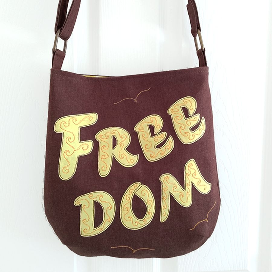 Brown ‘FREEDOM’ crossbody bag with yellow lettering and adjustable strap