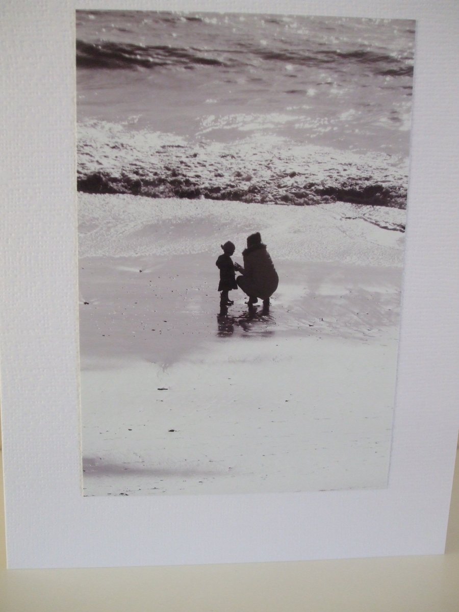 Black and white photo of a mother and child on a beach in Winter sunshine.