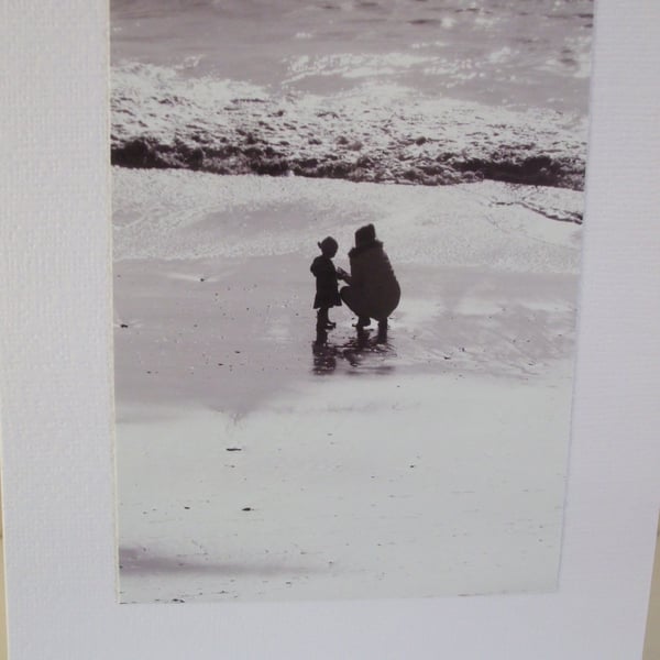 Black and white photo of a mother and child on a beach in Winter sunshine.